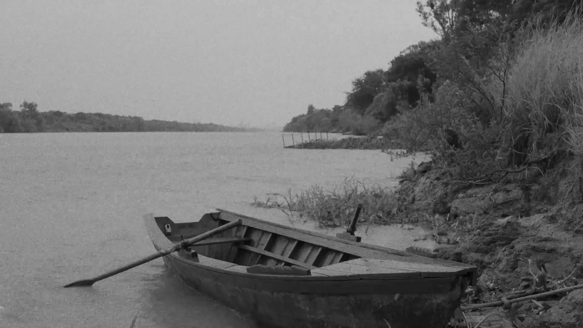 Bote de madera junto a la orilla de un río, en blanco y negro